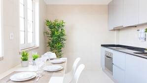 Une cuisine moderne avec des meubles blancs, un four encastré et un coin repas avec une table dressée pour quatre personnes.