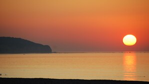 Un coucher de soleil sur une mer calme, avec la silhouette d’une colline en arrière-plan.