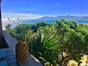 A patio with a view of the sea and sailboats, surrounded by green plants and a decorative vase. - MyHome Riviera Apartments - Cannes Rentals (Cannes)