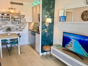 Uma cozinha moderna com máquina de lavar louça embutida, área de jantar com mesa e cadeiras, TV na parede e parede decorativa com padrão geométrico.