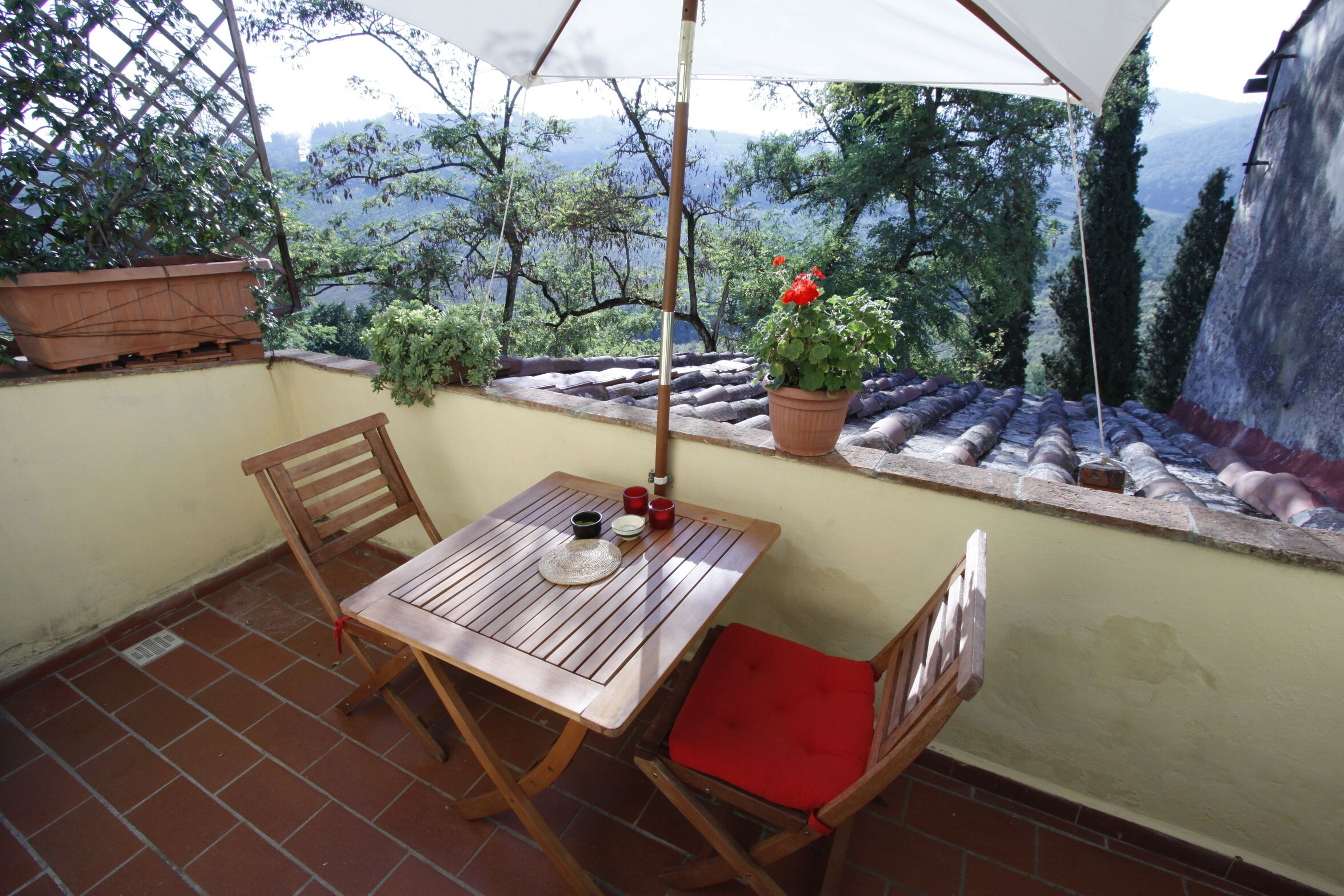 Une table et des chaises en bois sur une terrasse carrelée, avec vue sur les arbres et les montagnes.
