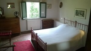 Ein Schlafzimmer mit einem Einzelbett, einem Schminktisch, einem Stuhl, einem Heizkörper und einem Fenster mit geöffneten Rollläden.