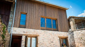 A two-story stone building with wooden exterior walls, large windows, and a balcony. - Old era of the 19th century Detached rural house Era del Mestre (Erinyà)