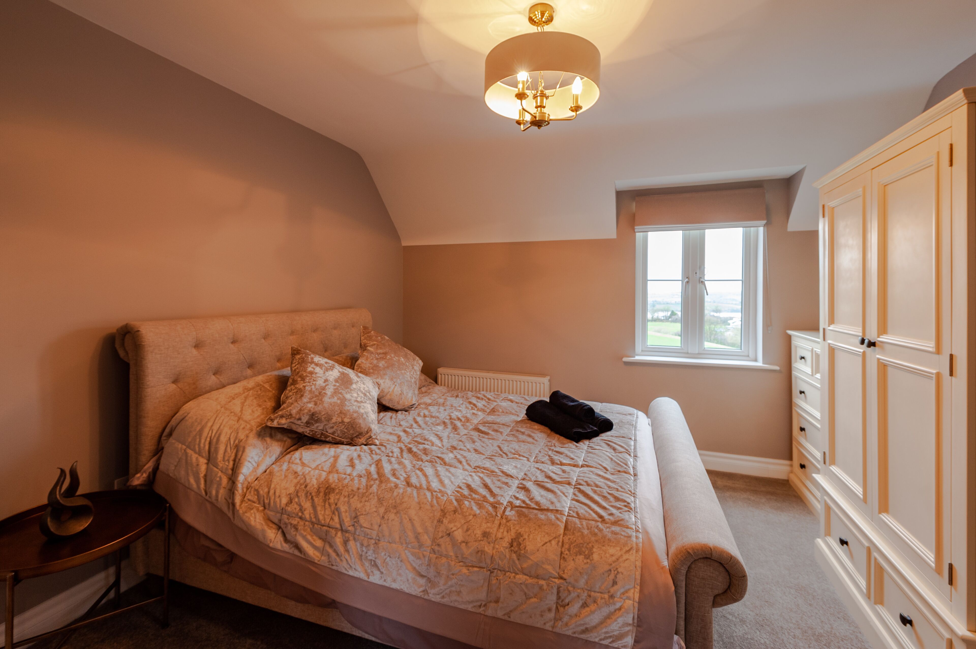 A bedroom with a large bed, a nightstand, a dresser, and a window with a view.