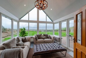 A conservatory with a high ceiling, large windows, a sofa, a bench, and a potted plant.