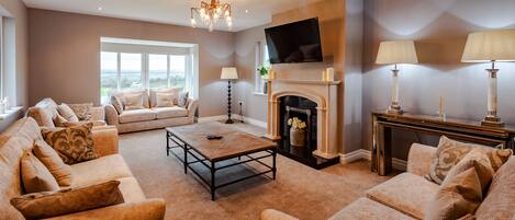 A spacious living room with a fireplace, a large window, and a television mounted on the wall.