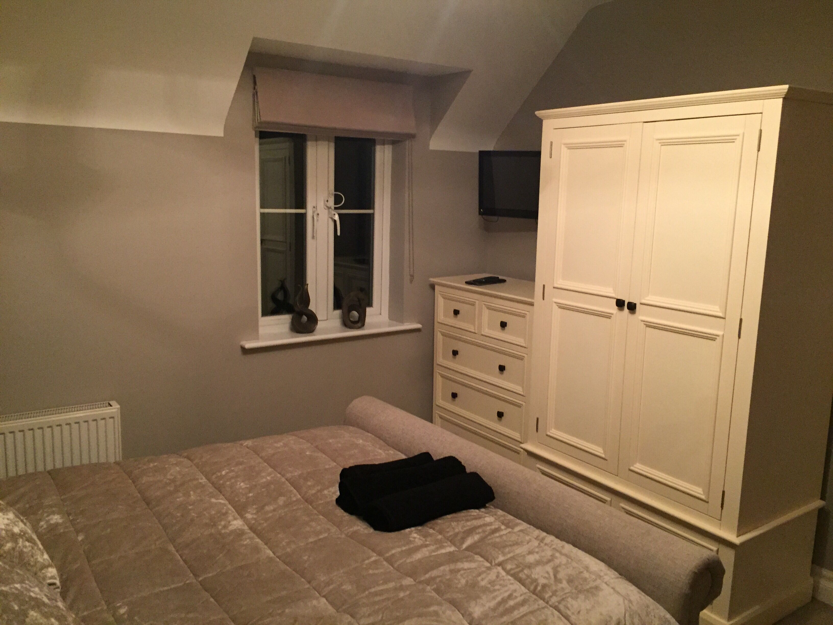 Een slaapkamer met een bed, een dressoir, een raam en een televisie.