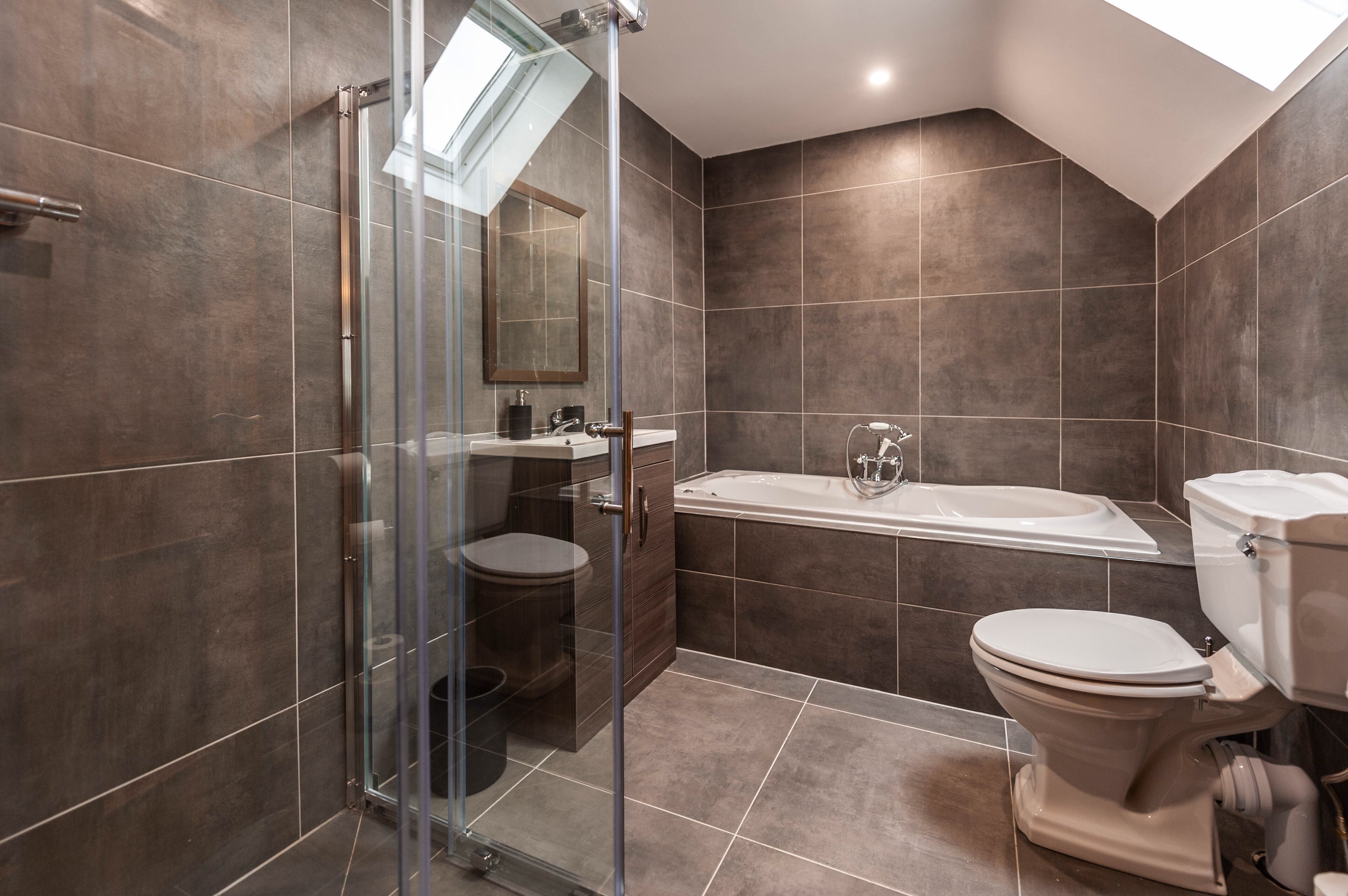 A modern bathroom with a glass shower enclosure, a bathtub, and a toilet.