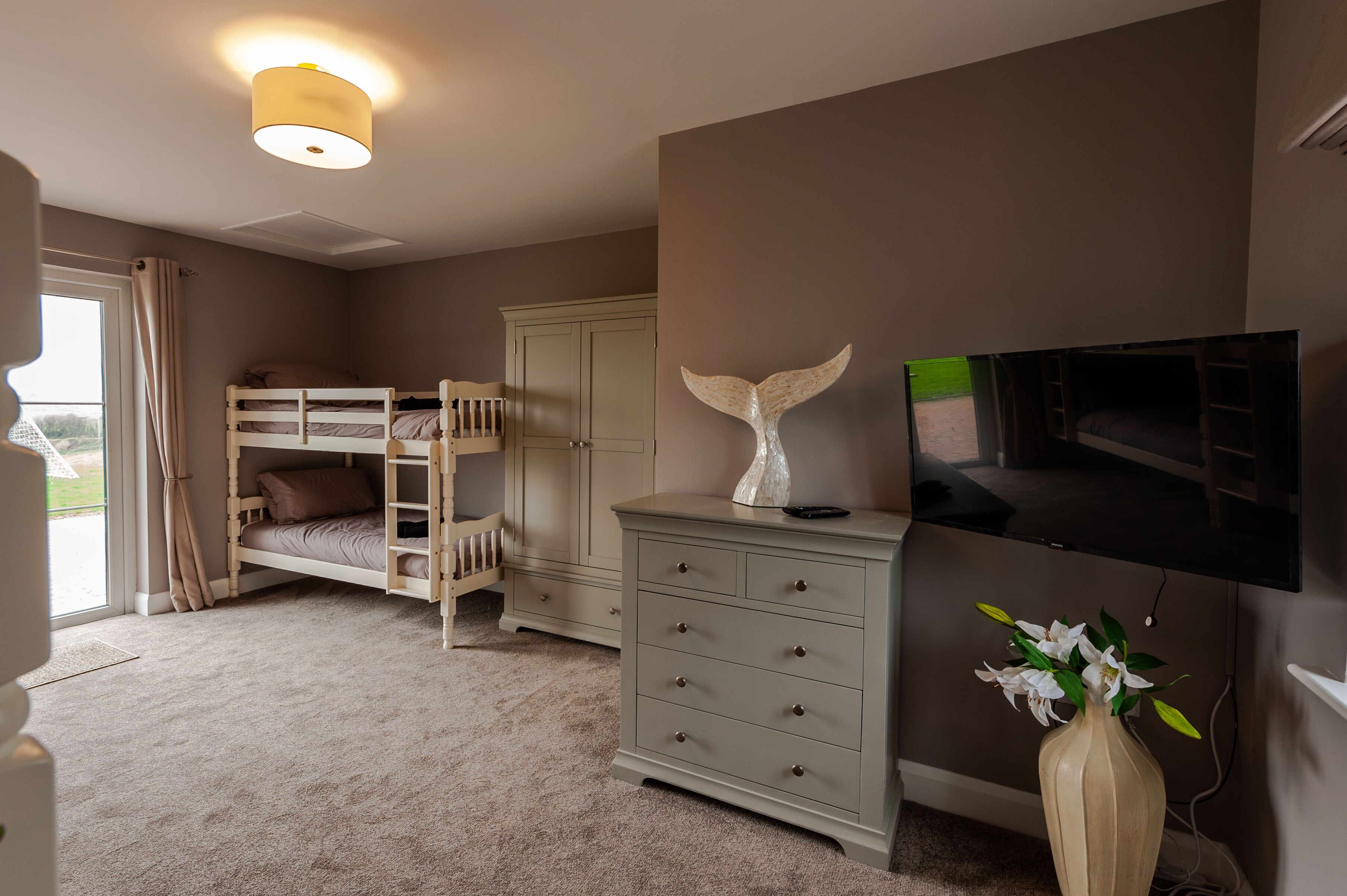 Een slaapkamer met stapelbedden, een dressoir, een televisie en een vaas met bloemen.