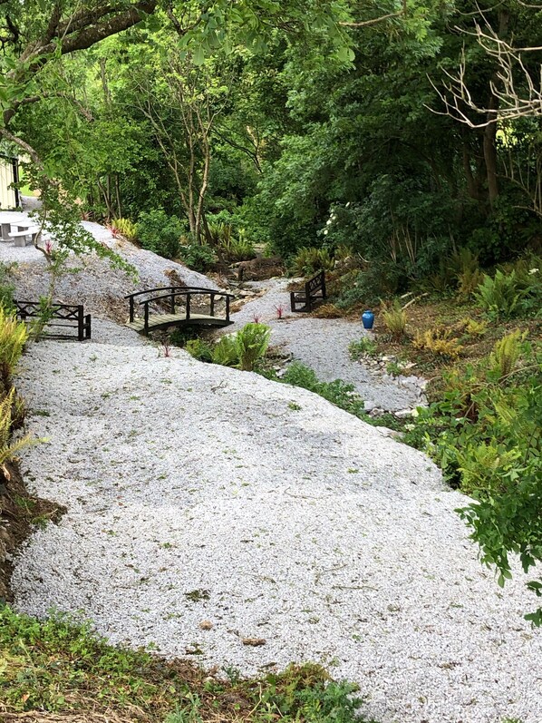 A gravel path with benches and a small bridge in a wooded area.