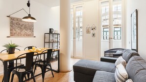 A modern living room with a wooden dining table, black chairs, a grey sofa, and a black hanging lamp.
