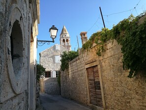 A narrow street with stone buildings, a bell tower, and a wooden door.