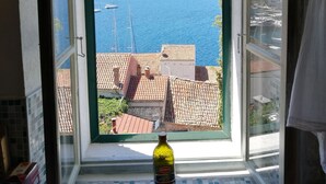 A window with a view of a coastal town, a bottle of olive oil on the windowsill, and a tiled floor. - Buena Vista Apartment Vintage View (Vis)