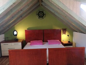 A bedroom with a sloped ceiling, a bed with two pillows, a bedside table with a lamp, and a wall-mounted mirror.