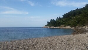 A pebble beach with a rocky shoreline and a forested hill in the background. - Buena Vista Apartment Vintage View (Vis)