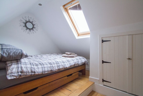 Une chambre dotée d’une lucarne, d’un lit recouvert d’une couette à carreaux, d’un banc en bois, d’un miroir fixé au mur et d’une armoire à porte blanche.