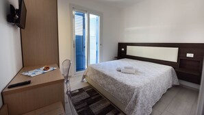 Ein Hotelzimmer mit einem Bett, einem Schreibtisch, einem Sessel, einem Fernseher und einer Schiebetür nach draußen.