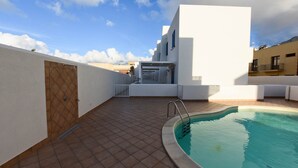 Ein Pool auf dem Dach mit gefliestem Deck, einer Holztür und einem weißen Gebäude im Hintergrund.