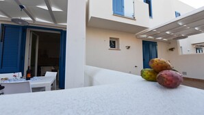 Ein weißer Tisch mit einer Flasche und Gläsern, ein kleines Fenster und eine blaue Tür.