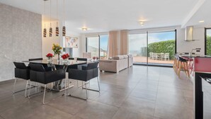 Ein modernes Wohnzimmer mit Essbereich, großen Fenstern und Blick auf Grünflächen.