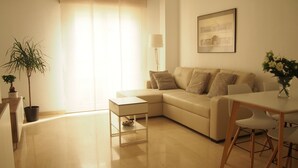 Una sala de estar con un sofá, una mesa de centro, una mesa de comedor con sillas, una lámpara y un cuadro en la pared.