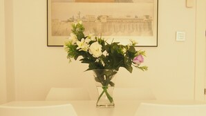 Un comedor con una mesa blanca, dos sillas blancas y un jarrón con flores.