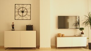 Una sala de estar moderna con un mueble blanco, un reloj decorativo de metal, un televisor de pantalla plana y una planta en maceta.
