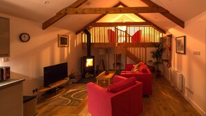 A cozy living room with a fireplace, red sofas, wooden beams, and a TV. - Stylish rural retreat with king-size comfort, close to Bude's stunning coastline (Bude)