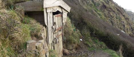 A rustic wooden structure with a door, situated beside a narrow, muddy path.