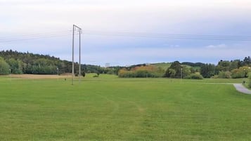 A large open grassy field with a tall metal structure, possibly a wind turbine, and a paved path curving through the landscape.