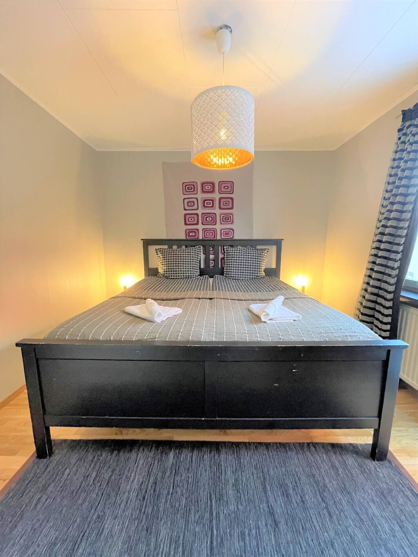 Un dormitorio con una cama grande, una lámpara colgante y una pared con diseños geométricos.