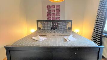 A bedroom with a large bed, a hanging light fixture, and a wall with geometric patterns.