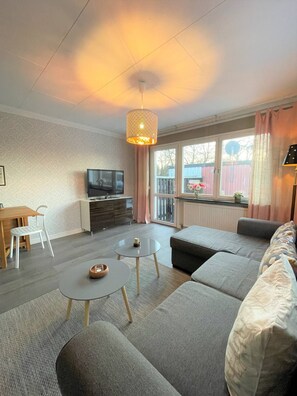 Ein modernes Wohnzimmer mit einer Couch, zwei runden Tischen, einem Fernseher und einem Balkon mit Blick.