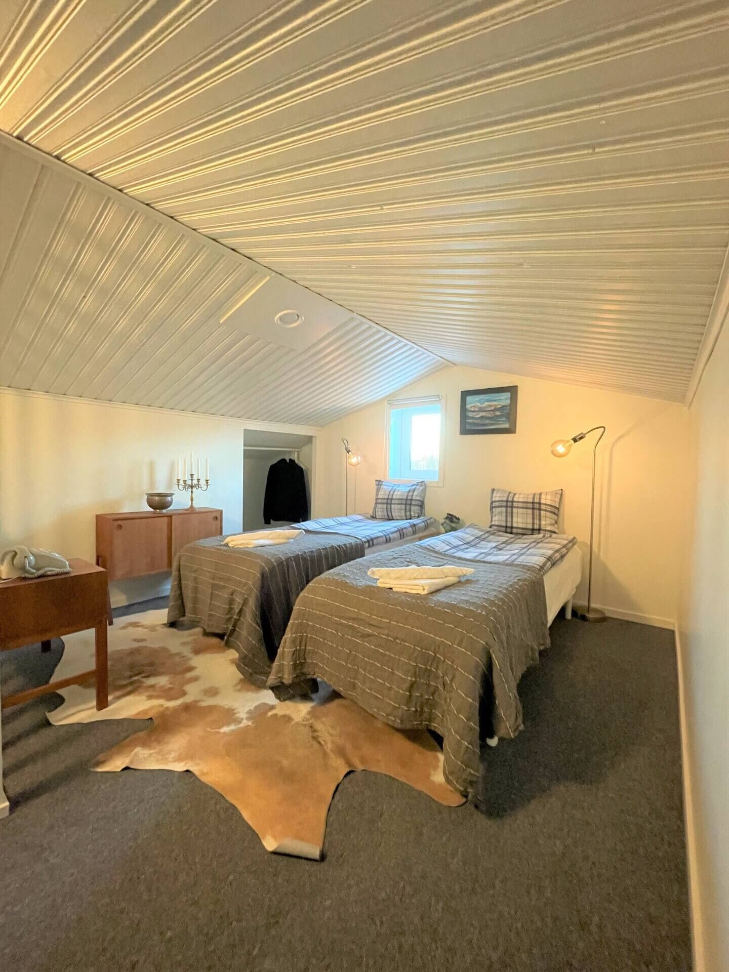 Een slaapkamer met twee bedden, een kleden van koeienhuid, een bureau en een raam.