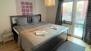 Un dormitorio con una cama, una mesita de noche, una lámpara de pared y un ventanal con cortinas.