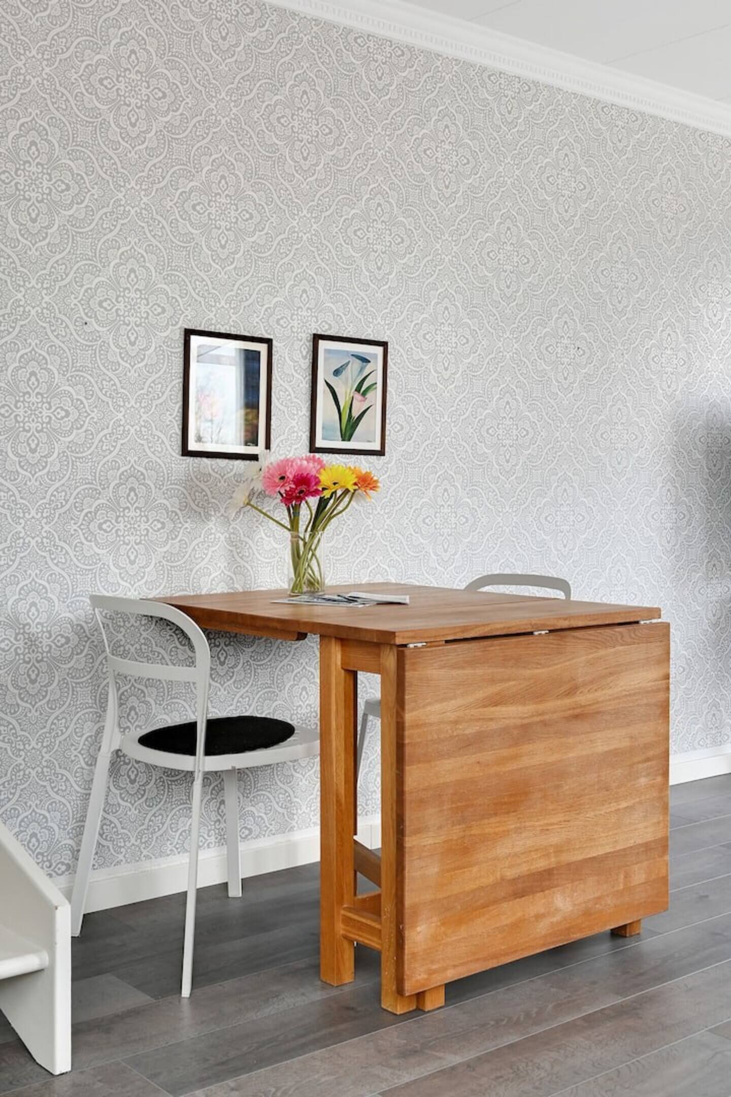 Uma sala de jantar com uma mesa de madeira, cadeiras brancas e papel de parede estampado.