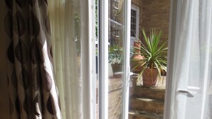 Ein Zimmer mit einer Schiebetür und Glasfront, die auf eine Ziegelwand hinausführt. Vor dem Fenster befindet sich ein gemustertes Vorhang, und auf dem Boden liegt ein Teppich.