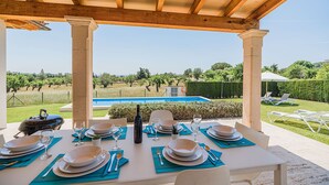 An outdoor dining area with a view of a pool and landscaped garden. - Villa Can Salat Selva (Selva)