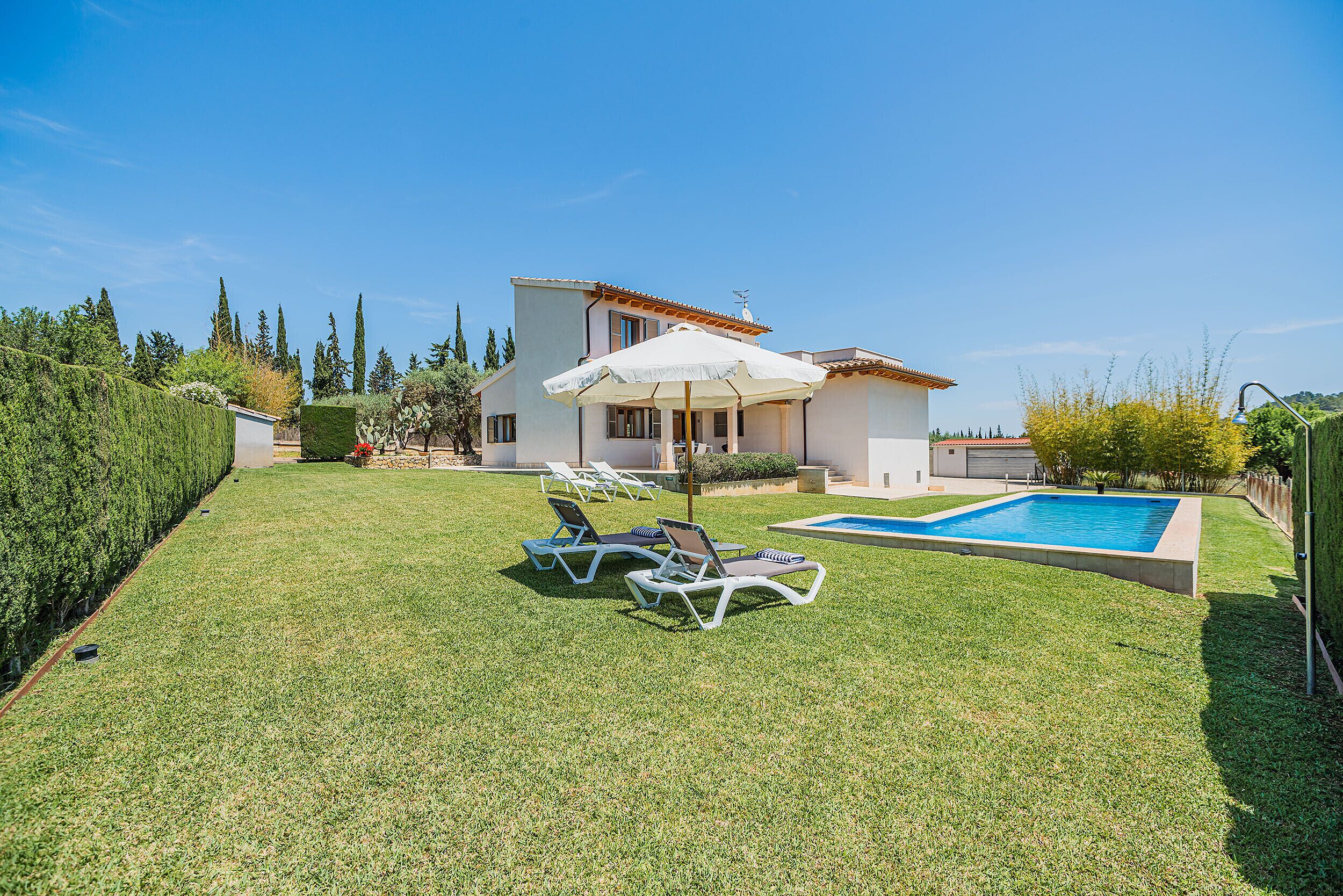 Une maison moderne avec une piscine, deux chaises longues et un grand parasol.