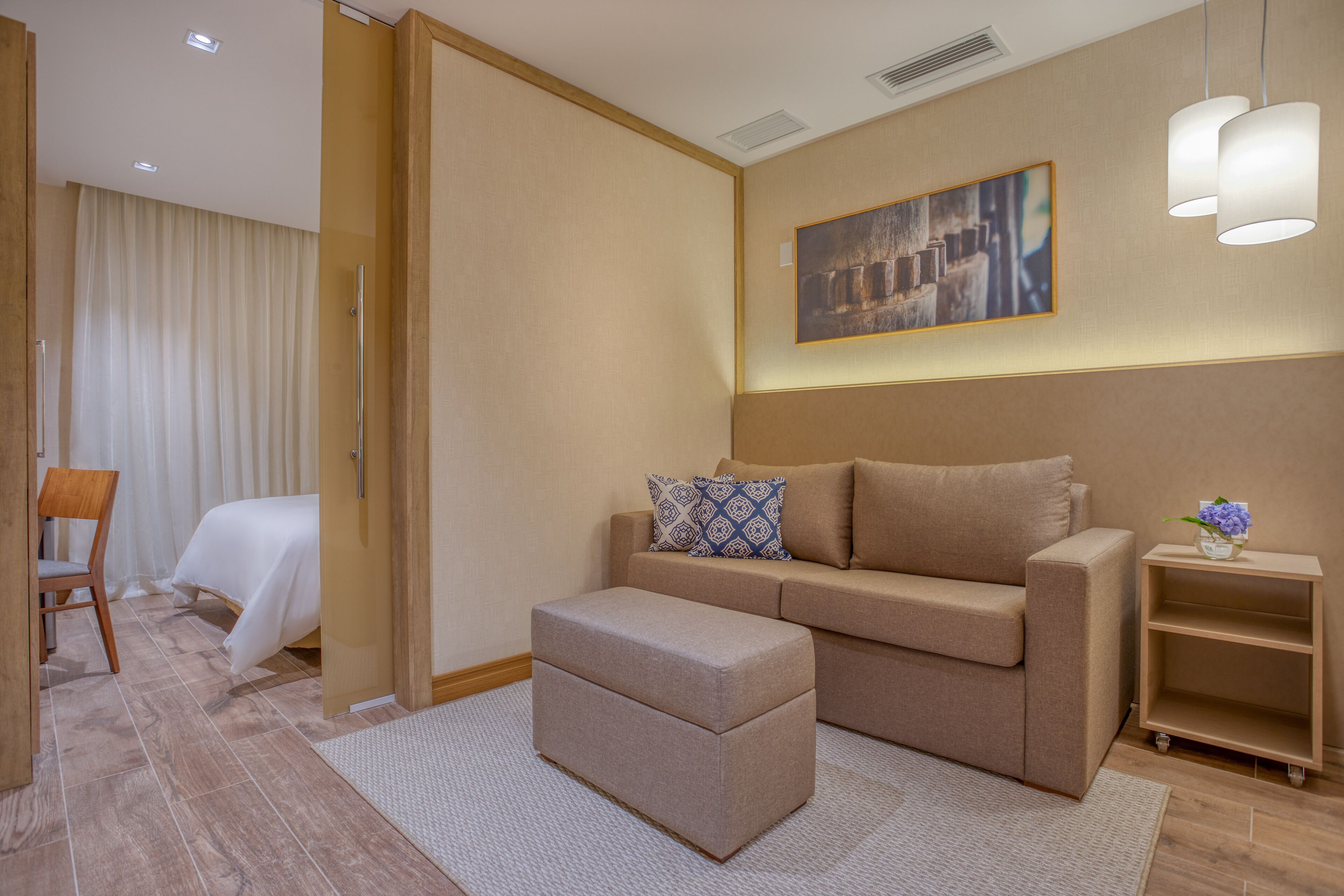 Una habitación de hotel moderna con un sofá, un reposapiés y una mesita auxiliar con un florero.