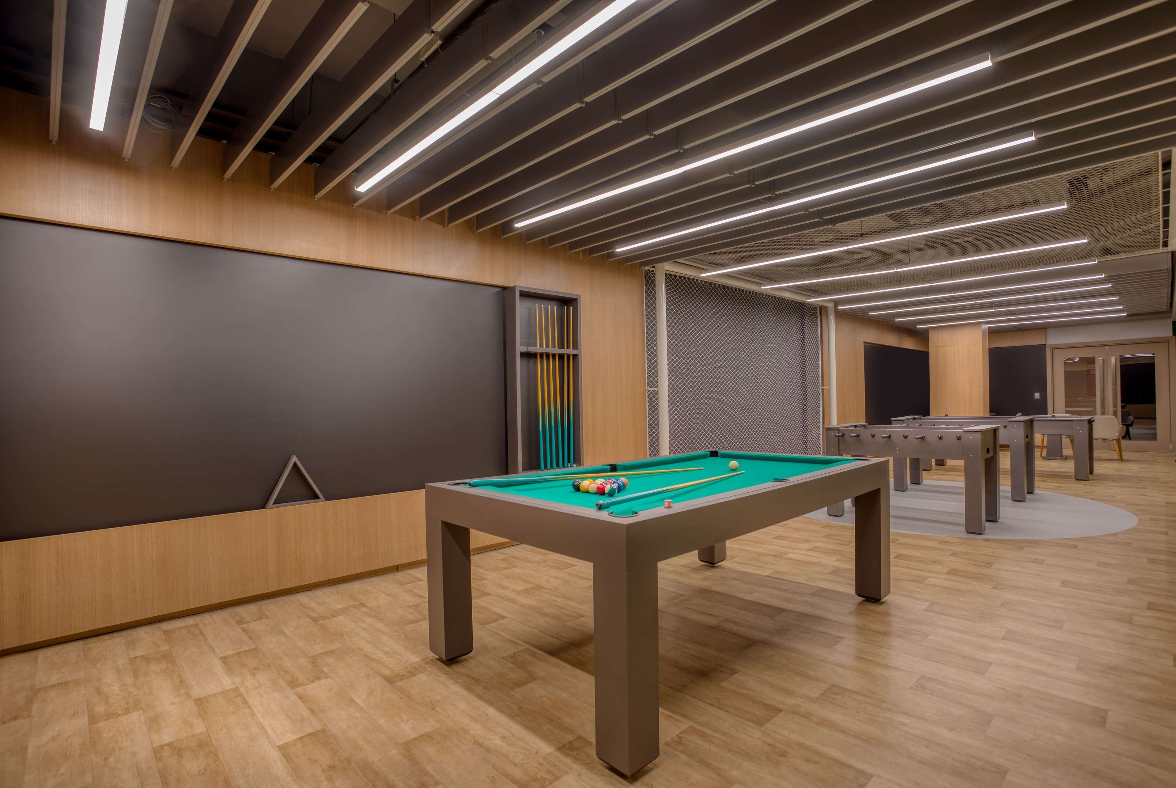 Uma área de lazer moderna em ambientes internos com mesa de bilhar, mesa de pebolim e tela de projeção.