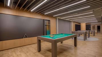 Uma área de lazer moderna em ambientes internos com mesa de bilhar, mesa de pebolim e tela de projeção.