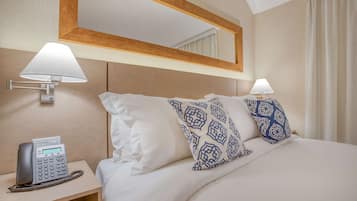 Habitación de hotel con cama, dos almohadas estampadas, lámpara de noche, teléfono y espejo sobre la cama.