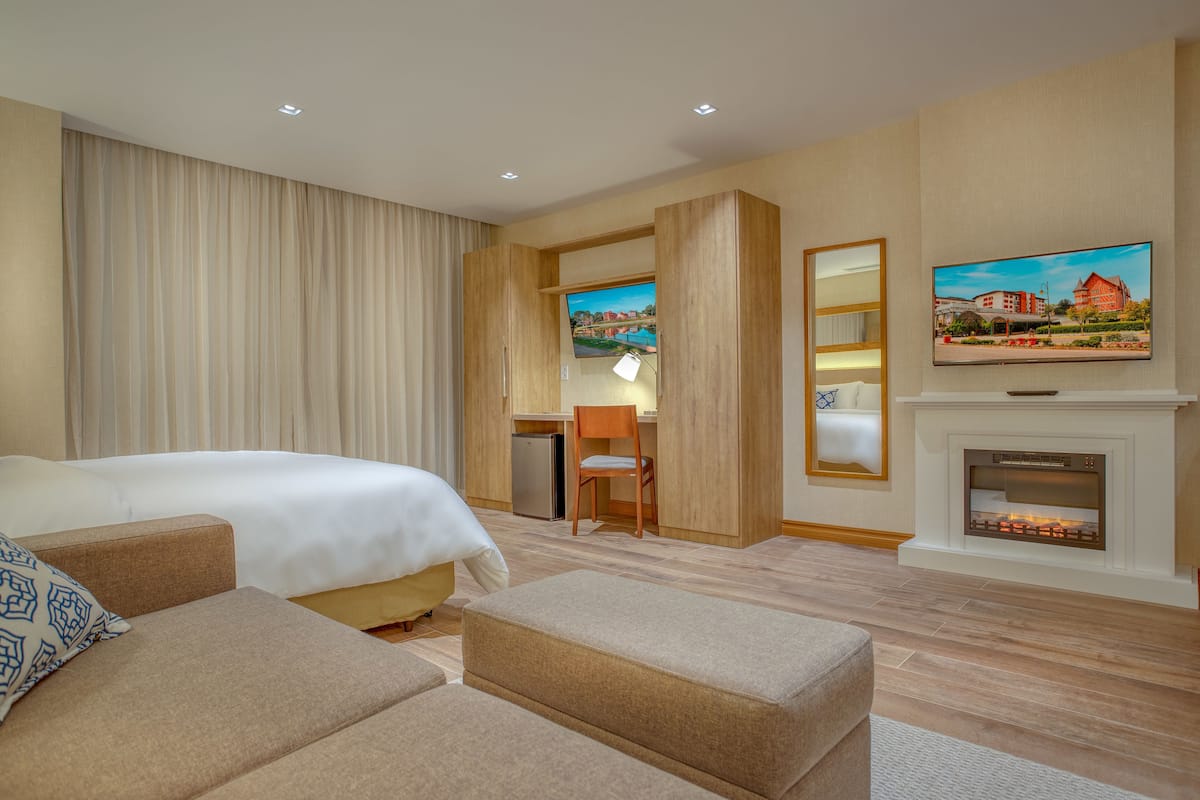 A hotel room with a bed, a sofa, a desk, a television, and a fireplace.