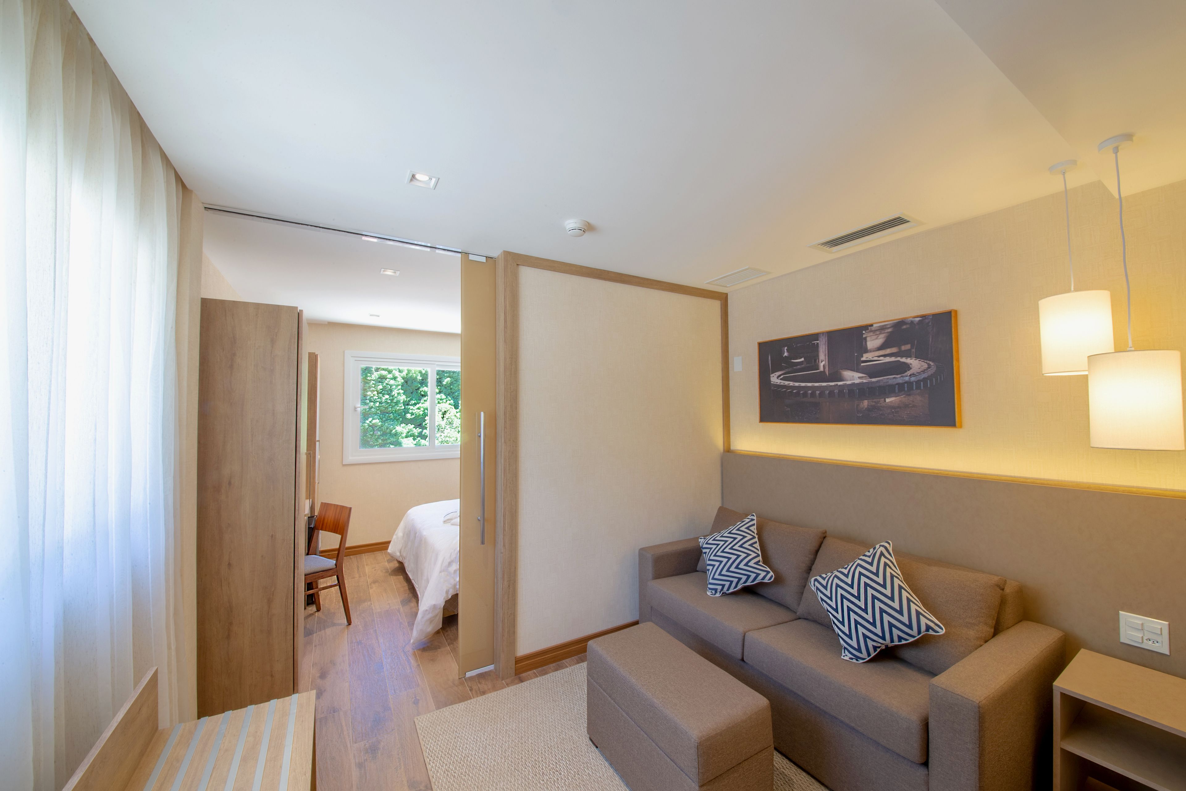 A modern hotel room with a sofa, ottoman, and a bed.
