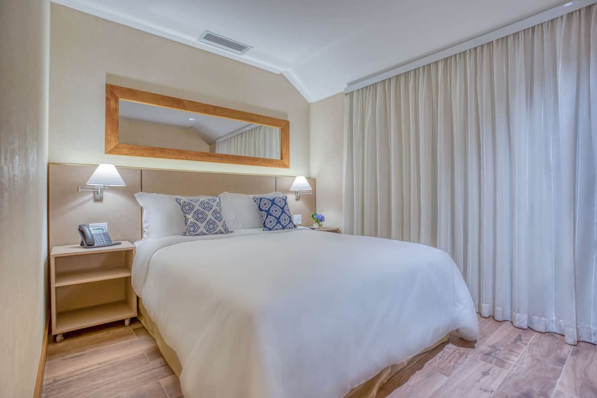 A hotel room with a large bed, two bedside tables with lamps, a telephone, and a mirror above the bed.