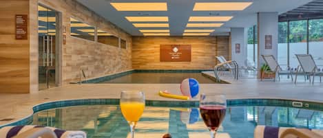 A poolside area with a table set for a meal, a glass of orange juice, and a glass of red wine.