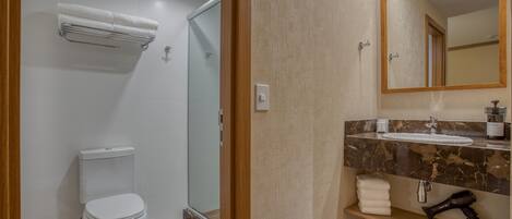 Un baño moderno con inodoro, ducha y tocador con lavamanos y espejo.