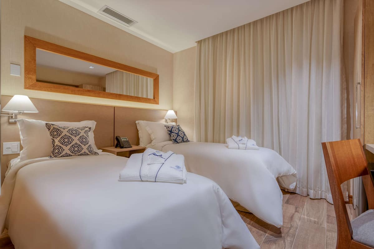 A hotel room with two beds, a large mirror, a wooden chair, and a nightstand with a lamp.