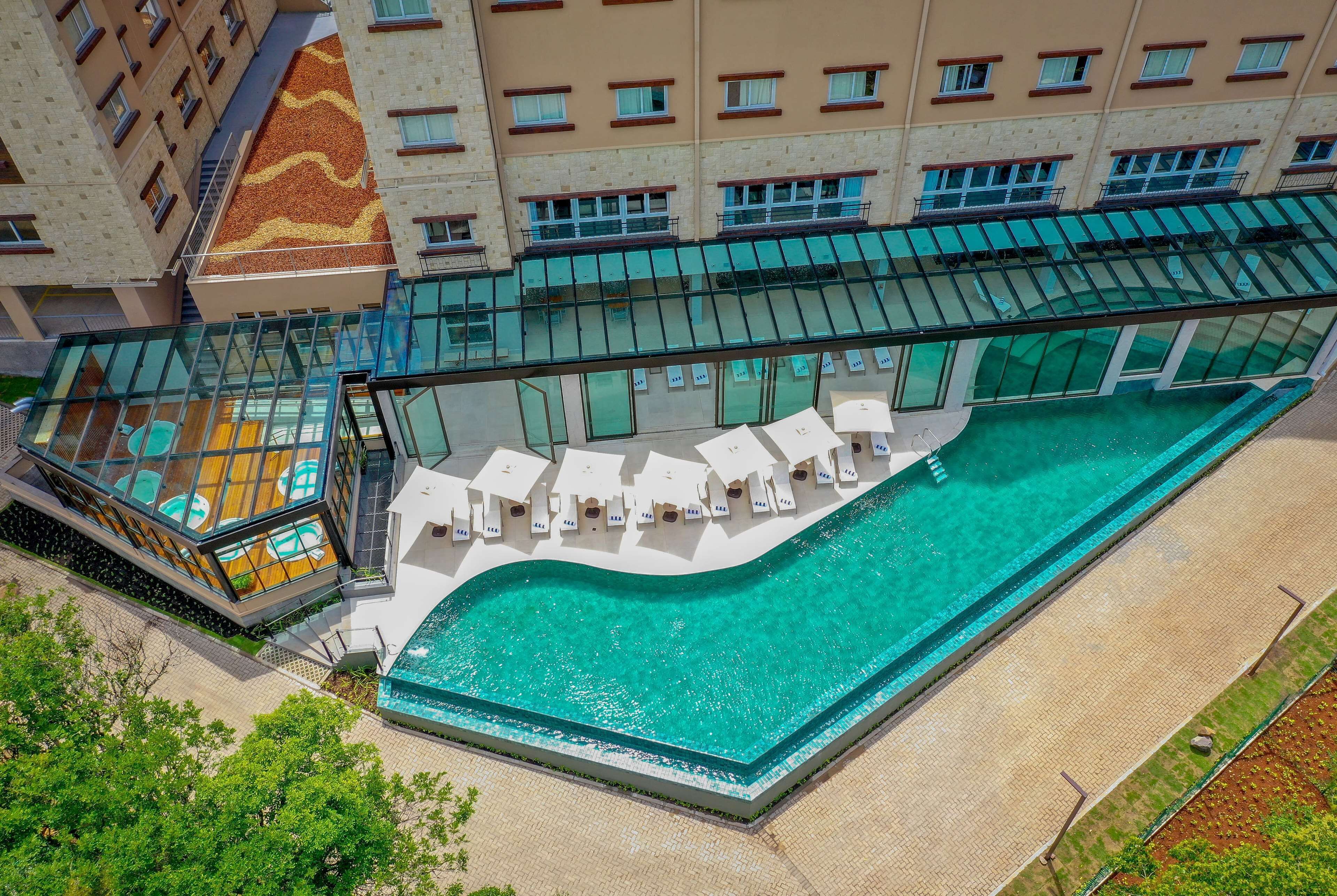 Vista aérea de un hotel con piscina, sillas de descanso y una terraza con paredes de vidrio.